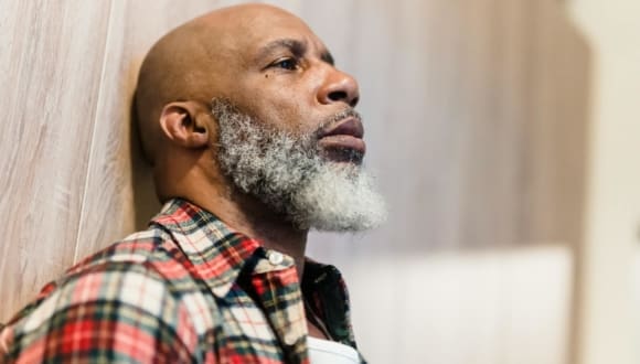 Close-up of a bearded African American man in plaid shirt looking pensive.